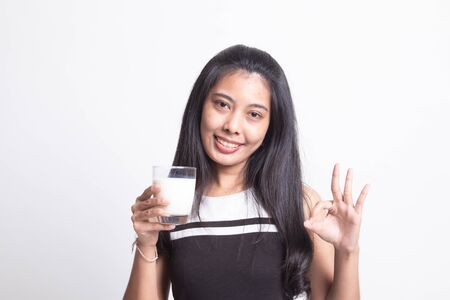 Healthy Asian woman drinking a glass of milk show OK sign on white backgroundの写真素材