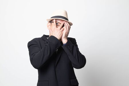 adult asian man peeking through fingers on white backgroundの写真素材