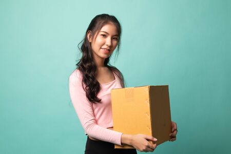 Delivery, relocation and unpacking.  young asian woman holding cardboard box on cyan backgroundの写真素材