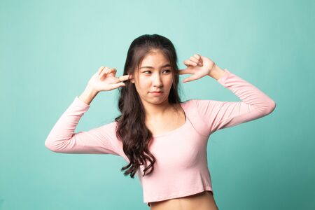 Young Asian woman block both ears with finger on cyan backgroundの写真素材