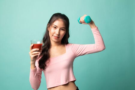 Young healthy Asian woman with dumbbell and  tomato juice on cyan backgroundの写真素材