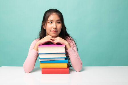 Happy young Asian woman read a book with books on table on cyan backgroundの写真素材