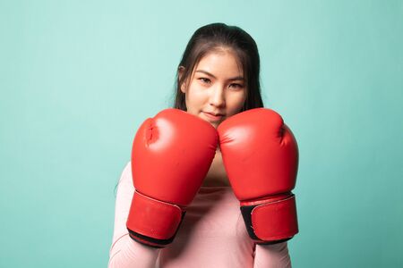 Young Asian woman with red boxing gloves on cyan backgroundの写真素材