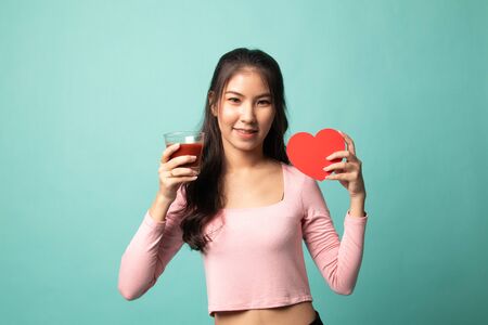 Young Asian woman with tomato juice and red heart on cyan backgroundの写真素材