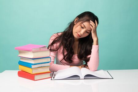 Exhausted Young Asian woman read a book with books on table on cyan backgroundの写真素材