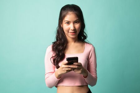 Young Asian woman with mobile phone on cyan backgroundの写真素材