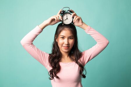 Young Asian woman smile with a clock on cyan backgroundの写真素材