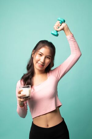 Healthy Asian woman drinking a glass of milk and dumbbell on cyan backgroundの写真素材