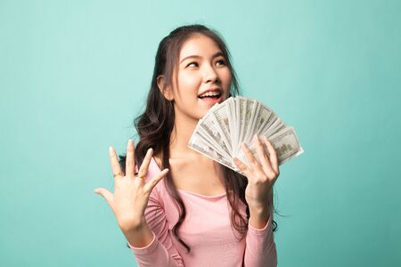 Portrait of  young asian woman  showing bunch of money banknotes on cyan backgroundの写真素材