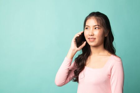Young Asian woman talking with mobile phone on cyan backgroundの写真素材