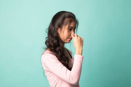 Young Asian woman  holding her nose because of a bad smell on cyan backgroundの写真素材
