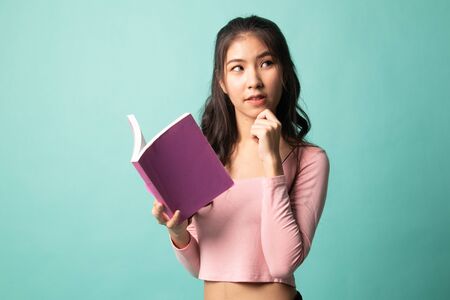 Young Asian woman with a book is thinking on cyan backgroundの写真素材