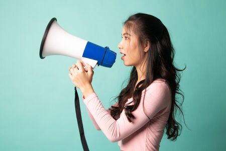 Beautiful young Asian woman announce with megaphone on cyan backgroundの写真素材