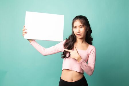 Young Asian woman point to  blank sign on cyan backgroundの写真素材