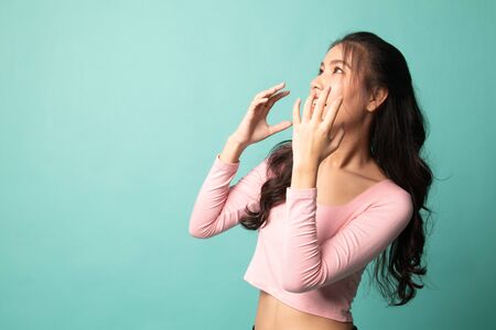 Beautiful young Asian woman shocked  and look up on cyan backgroundの写真素材