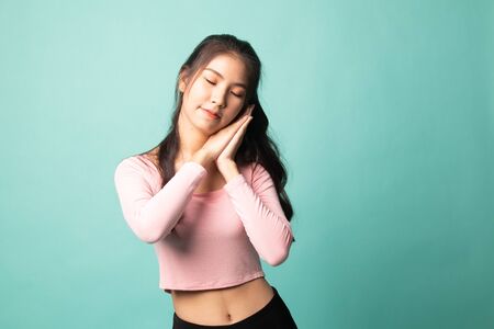 Beautiful young Asian woman with sleeping gesture on cyan backgroundの写真素材