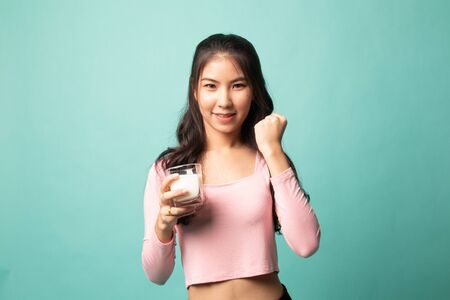 Healthy Asian woman drinking a glass of milk on cyan backgroundの写真素材