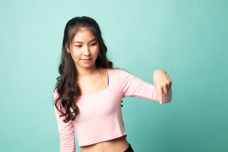 Beautiful young Asian woman point down to blank space on cyan backgroundの写真素材