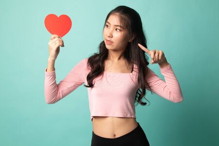 Asian woman point to red heart on cyan backgroundの写真素材