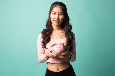 Young Asian woman with a pig coin bank on cyan backgroundの写真素材