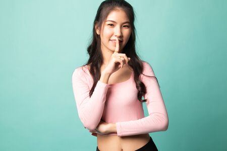 Asian girl smile show quite hand sign on cyan backgroundの写真素材