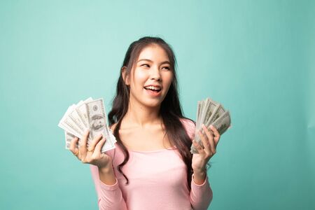 Portrait of  young asian woman  showing bunch of money banknotes on cyan backgroundの写真素材