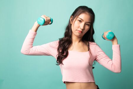 Exhausted Asian woman with dumbbells on cyan backgroundの写真素材