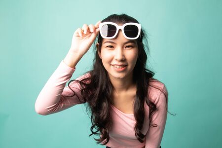 Portrait of a beautiful young asian girl in sunglasses on cyan backgroundの写真素材