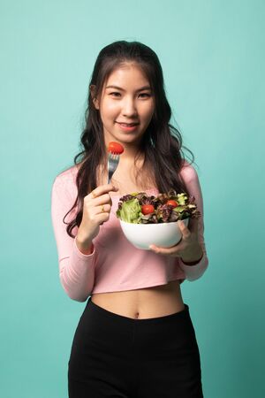 Healthy Asian woman with salad on cyan backgroundの写真素材