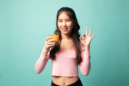 Young Asian woman drink orange juice show OK sign on cyan backgroundの写真素材