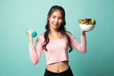 Healthy Asian woman with dumbbells and salad on cyan backgroundの写真素材