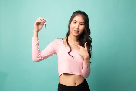 Cute asian girl showing home residence keys on cyan backgroundの写真素材
