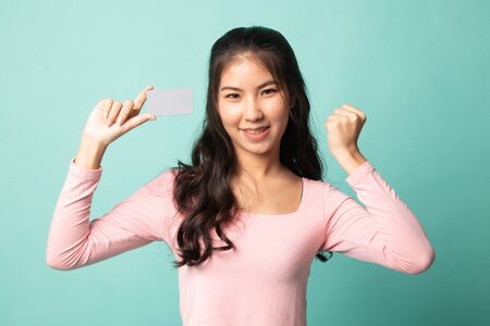 Young Asian woman fist pump with blank card on cyan backgroundの写真素材