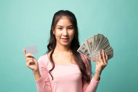 Portrait of  young asian woman  showing bunch of money banknotes on cyan backgroundの写真素材