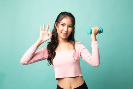 Healthy Asian woman show OK with dumbbells on cyan backgroundの写真素材