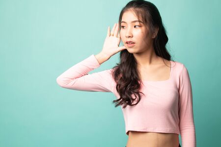 Beautiful young Asian woman listen to something on cyan backgroundの写真素材