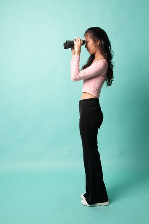 Full body of young Asian woman with binoculars on cyan backgroundの写真素材
