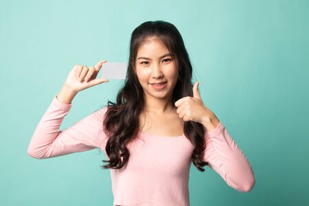 Young Asian woman thumbs up with a blank card on cyan backgroundの写真素材