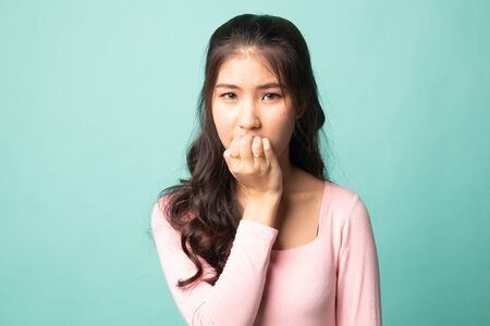 Unsure hesitant nervous young asian  woman biting her fingernails on cyan backgroundの写真素材