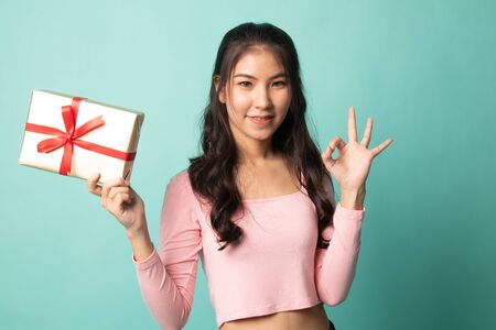 Young Asian woman show OK with a gift box on cyan backgroundの写真素材