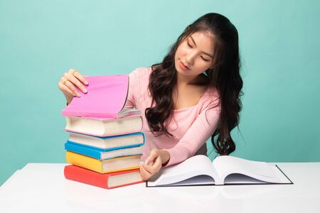 Young Asian woman read a book with books on table on cyan backgroundの写真素材