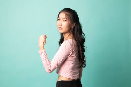 Young Asian woman turn back thumbs up on cyan backgroundの写真素材
