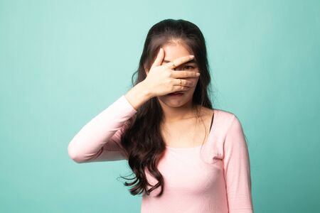 Beautiful young Asian woman peeking through fingers on cyan backgroundの写真素材