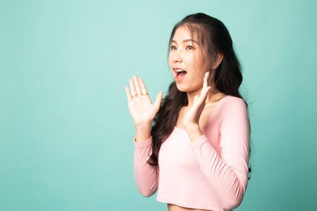 Young Asian woman is surprised and smile on cyan backgroundの写真素材
