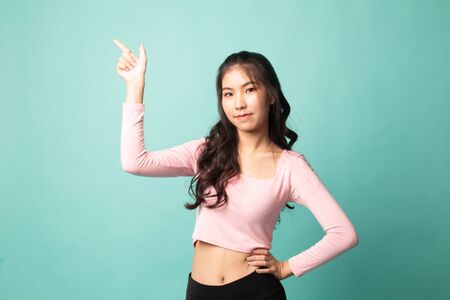 Young Asian woman smile and point on cyan backgroundの写真素材