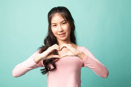 Young Asian woman show heart hand sign on cyan backgroundの写真素材