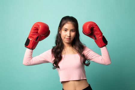 Young Asian woman with red boxing gloves on cyan backgroundの写真素材