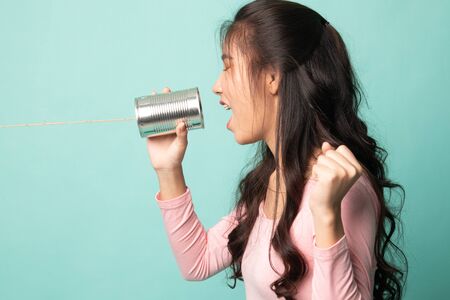 Young Asian woman shout with tin can phone on cyan backgroundの写真素材