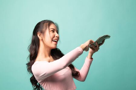 Portrait of very happy  young asian woman throwing out money banknotes on cyan backgroundの写真素材