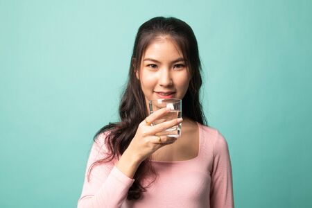 Young Asian woman with a glass of drinking water on cyan backgroundの写真素材